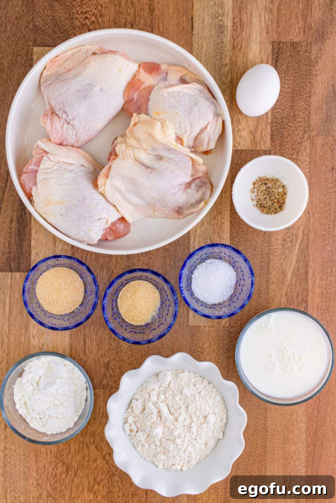 Ingredients needed: buttermilk, egg, all-purpose flour, cornstarch, garlic powder, onion powder, kosher salt, black pepper, bone-in chicken thighs and olive oil spray. All laid out on a wooden surface.