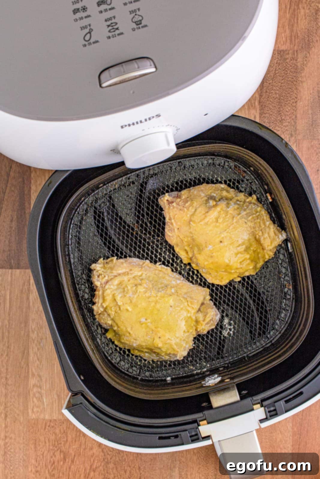 Chicken thighs in air fryer basket sprayed with olive oil spray. Raw, coated chicken ready for cooking.
