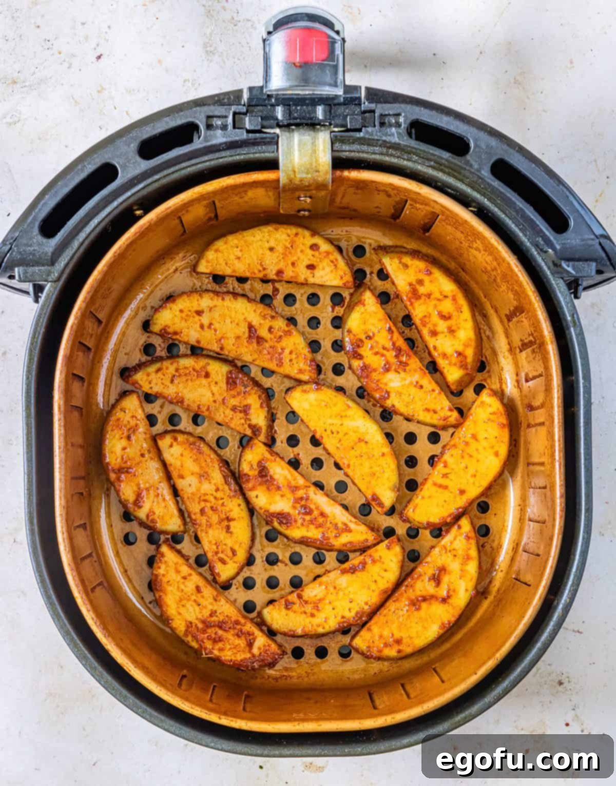 Coated potato wedges in air fryer basket.