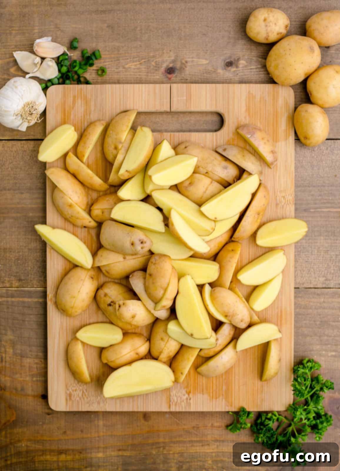 Golden Garlic Butter Chicken and Crispy Potatoes 6 Baby gold potatoes neatly cut into quarters on a wooden cutting board, ready for parboiling.