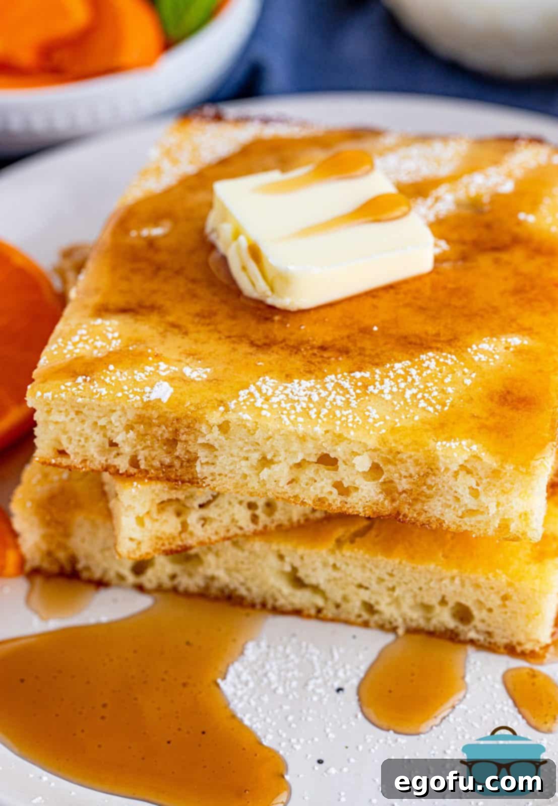 Three stacked slices of golden brown Sheet Pan Pancakes, drizzled with rich maple syrup and topped with a pat of melting butter.