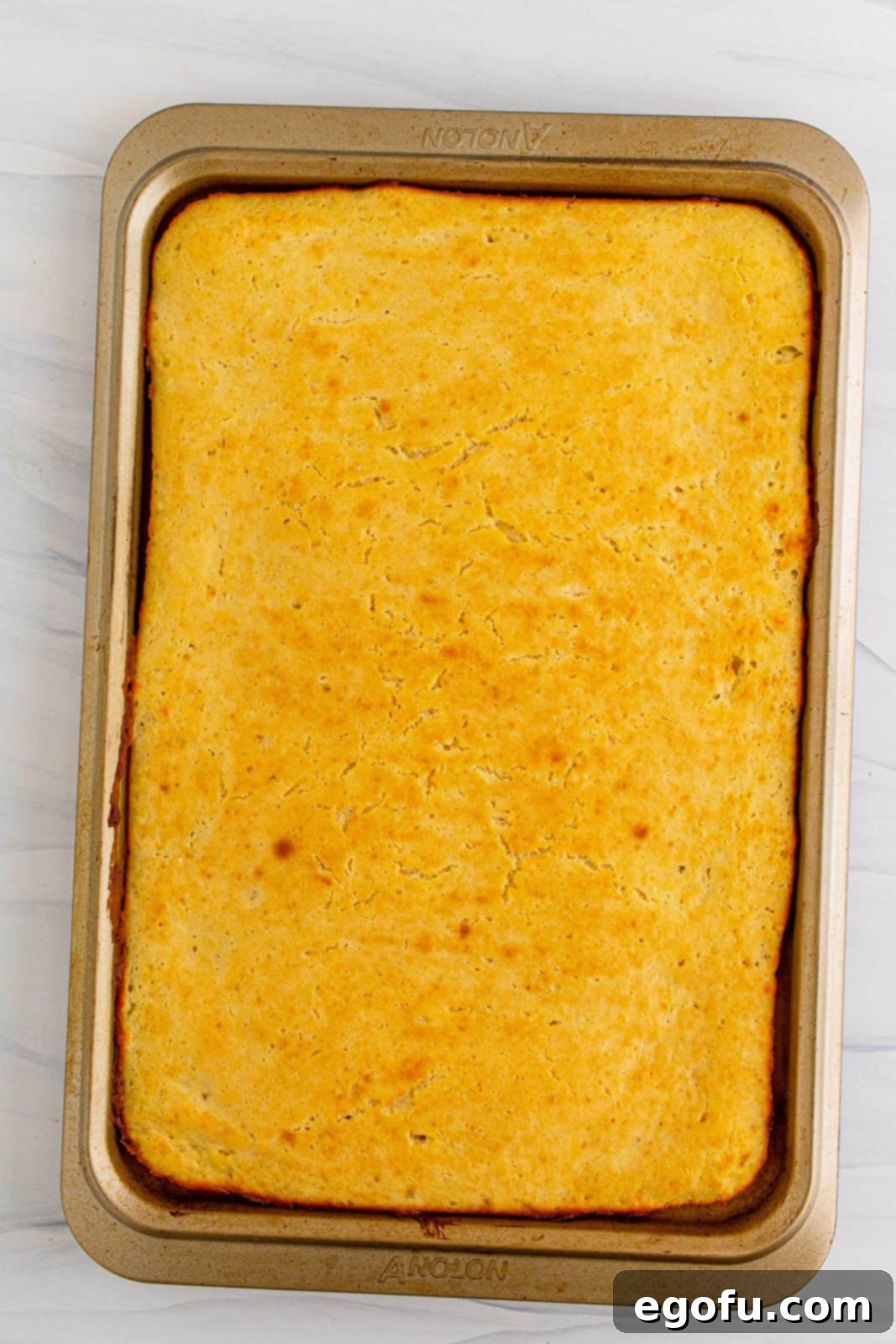 A freshly baked sheet of golden-brown Sheet Pan Pancakes sitting in the pan, just removed from the oven and ready to be sliced.