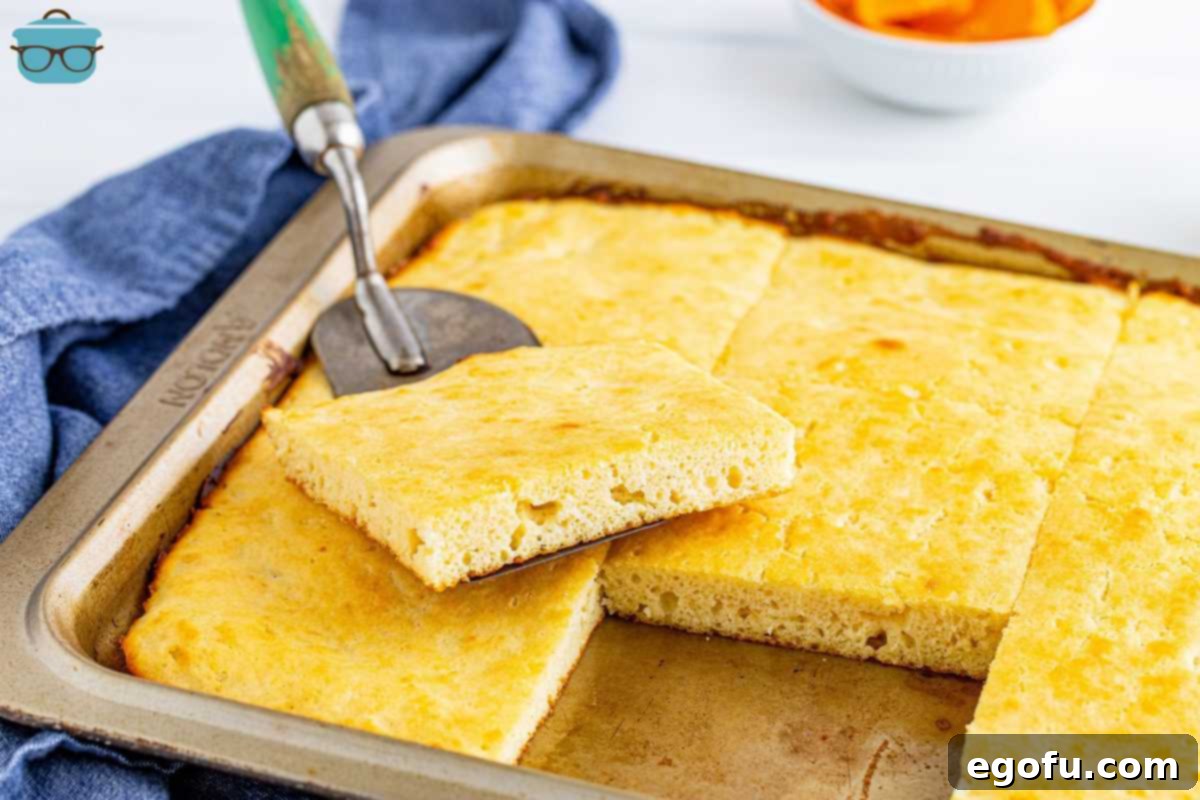 A spatula gently lifting out a perfectly baked slice of Sheet Pan Pancakes from the pan, revealing its fluffy texture.