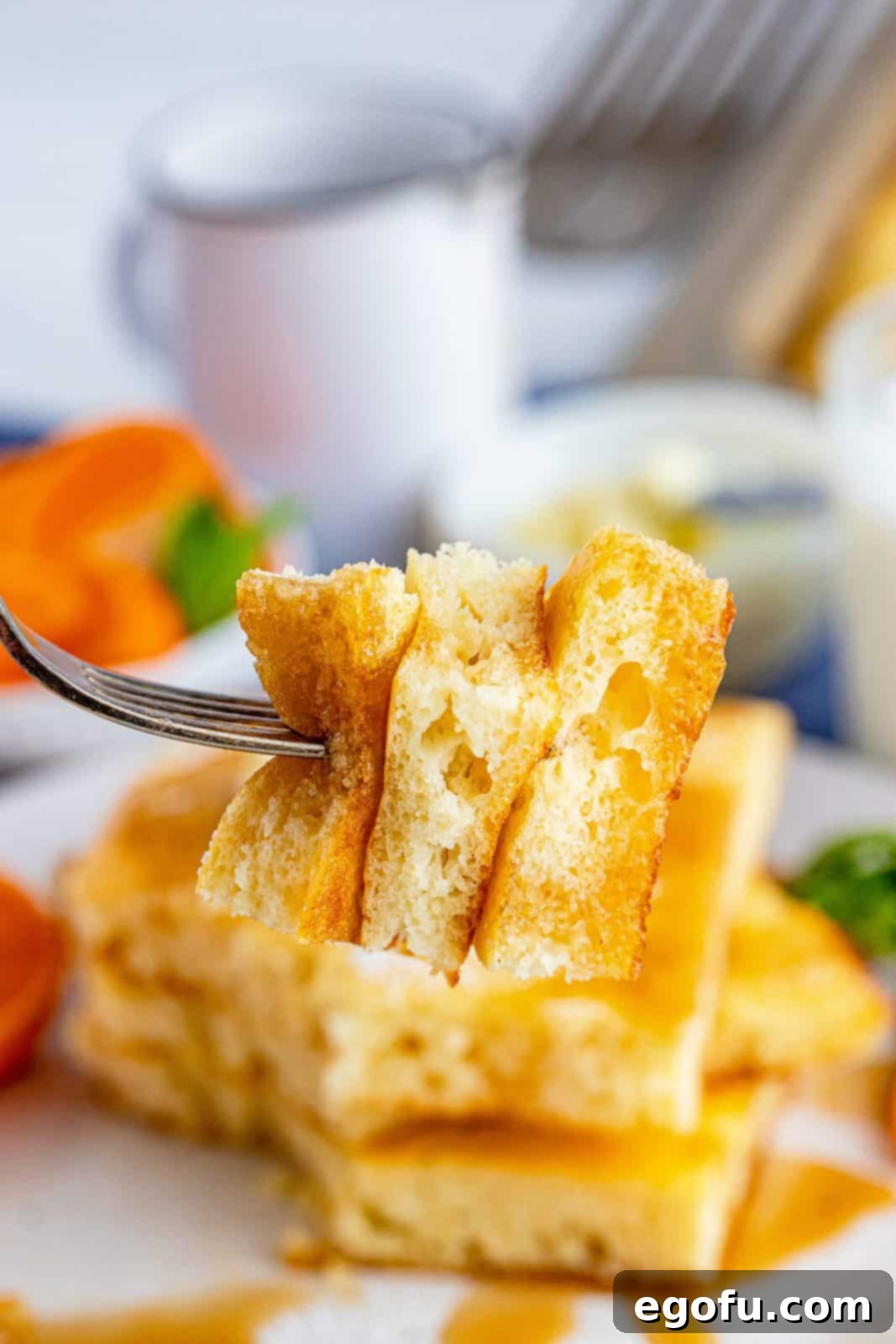A fork holding a bite-sized piece of fluffy sheet pan pancake, ready to be enjoyed with a hint of syrup.
