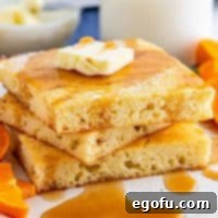 Square photo of three stacked Sheet Pan Pancakes with butter and syrup.