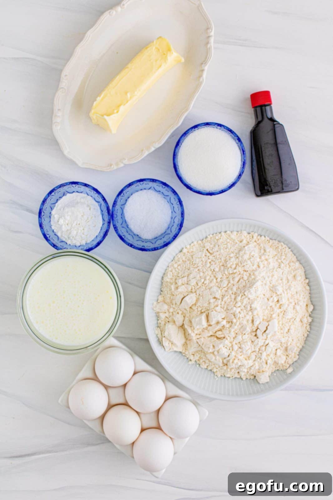 A beautifully arranged flat lay of all the essential ingredients for Sheet Pan Pancakes: golden salted butter, creamy buttermilk, fresh eggs, aromatic vanilla extract, all-purpose flour, fine granulated sugar, and baking powder.