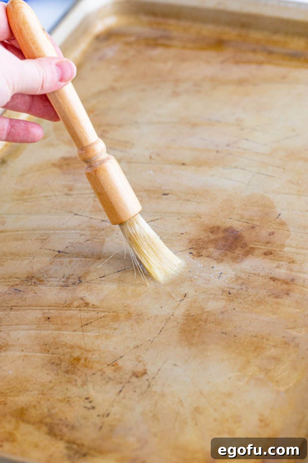 Melted butter being evenly brushed across the surface of a metal sheet pan, preparing it for the pancake batter.