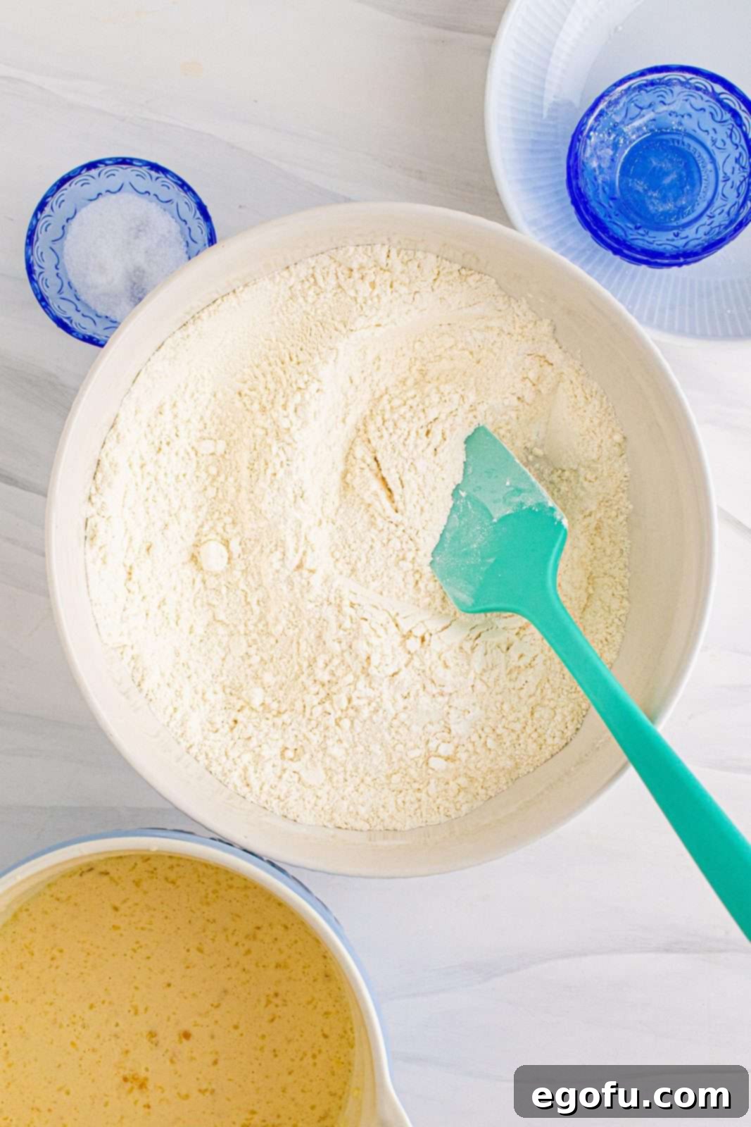Dry ingredients, including flour, sugar, and baking powder, being stirred together in a large white mixing bowl.
