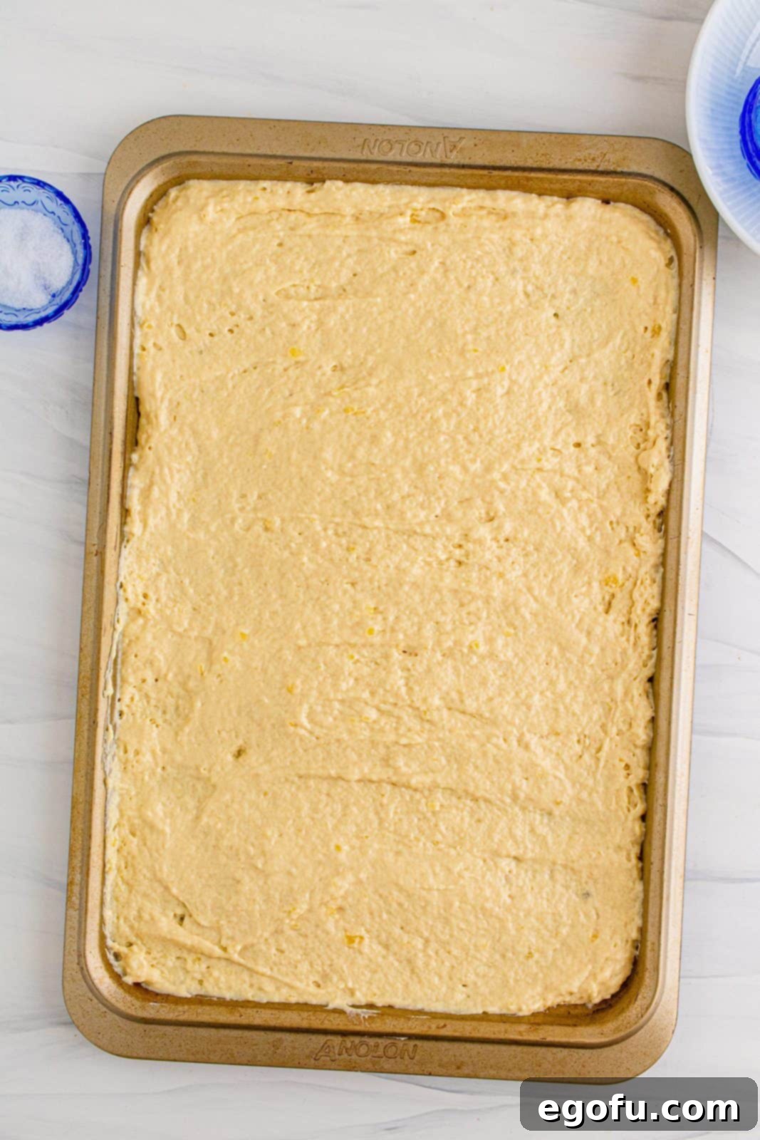 Smooth pancake batter meticulously spread into an even layer on a buttered sheet pan, ready for baking.