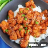 Square image of Easy General Tso's Chicken served over white rice, garnished with sesame seeds and scallions for a beautiful presentation.