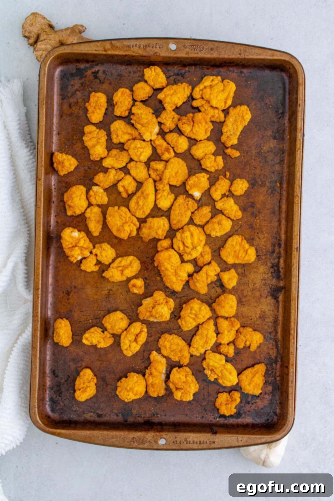 Popcorn chicken spread out on a baking pan, ready to be cooked until golden and crispy according to package instructions.