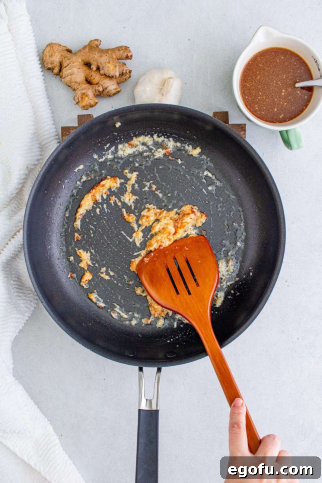 Minced garlic, fresh ginger, and chili paste sizzling in hot vegetable oil in a sauté pan, being stirred constantly to release their aromatic flavors before the sauce is added.