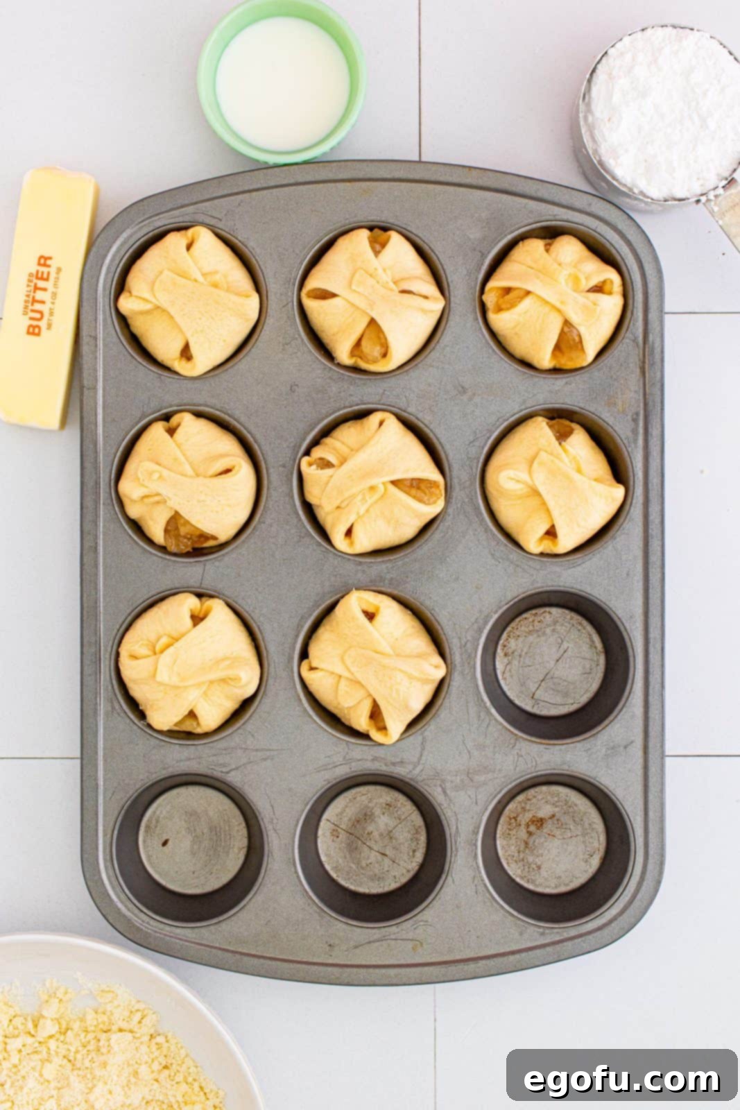 Quick Apple Pie Bites 11 Crescent dough squares folded over the apple pie filling in the muffin tin, forming small cups.
