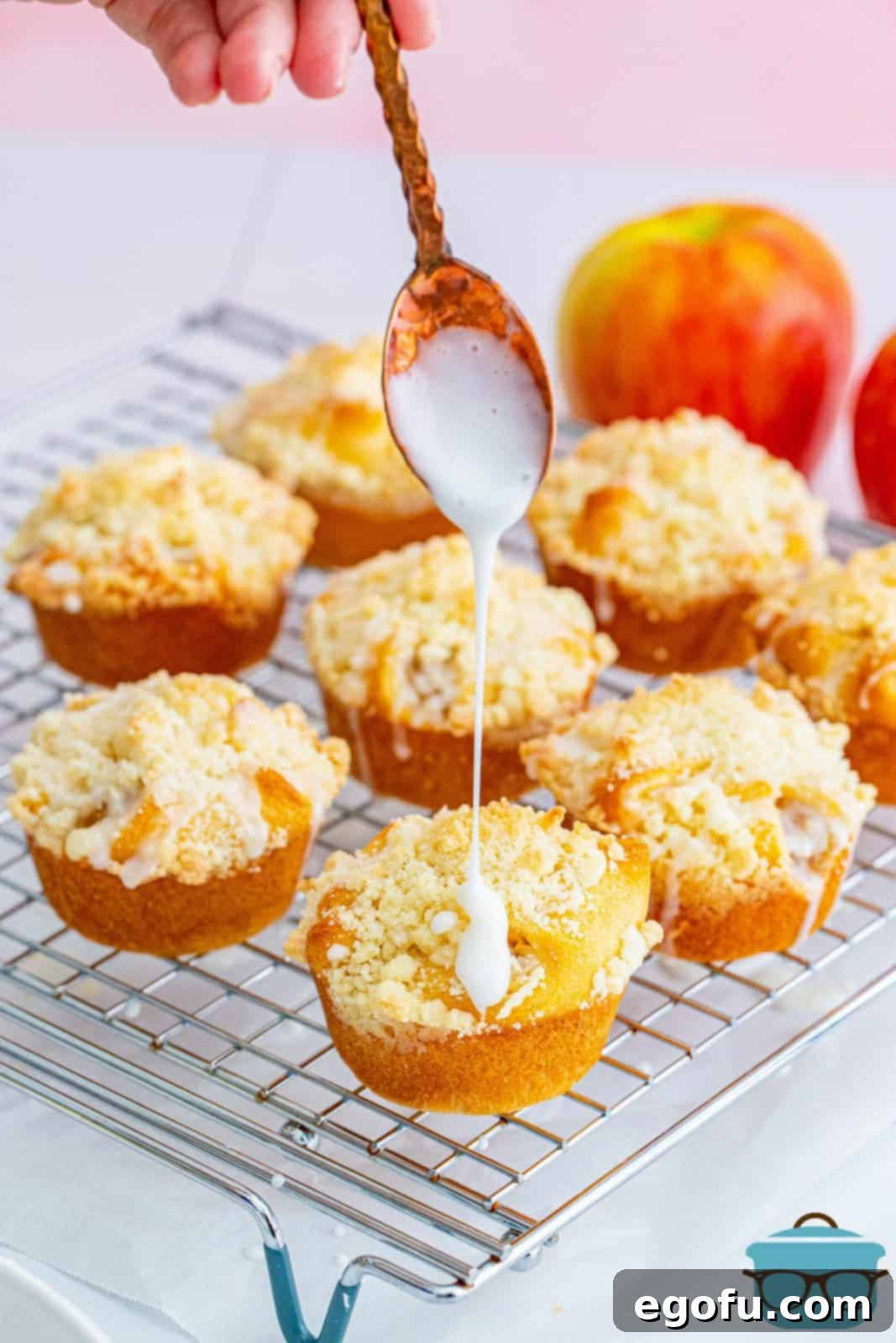 Quick Apple Pie Bites 14 A spoon drizzling white glaze over warm Easy Apple Pie Cups arranged on a wire rack, enhancing their visual appeal.