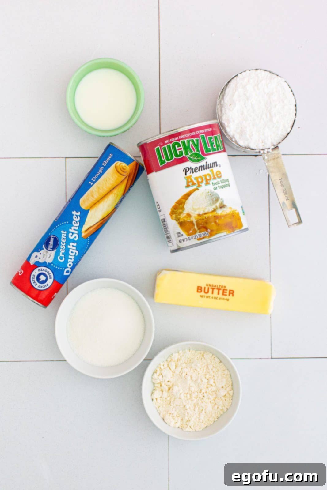 Quick Apple Pie Bites 4 Ingredients needed for Easy Apple Pie Cups: a can of apple pie filling, granulated sugar, all-purpose flour, unsalted butter, a tube of crescent roll dough, powdered sugar, and a carton of whole milk.