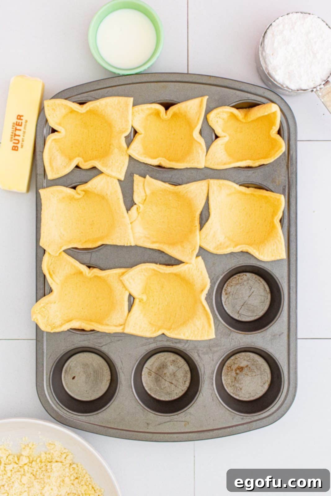 Quick Apple Pie Bites 9 Crescent dough squares individually pressed into the sections of a prepared muffin tin, ready for filling.