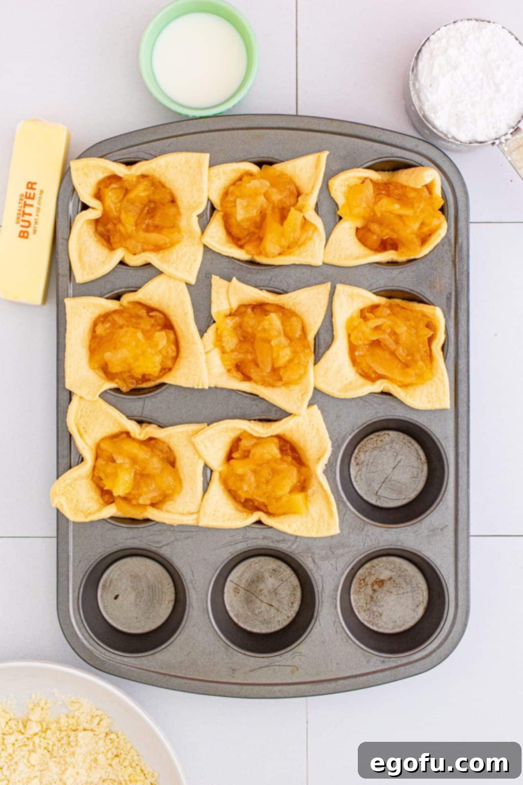 Quick Apple Pie Bites 10 Apple pie filling evenly added to each crescent square in the muffin tin, ready for the next step.