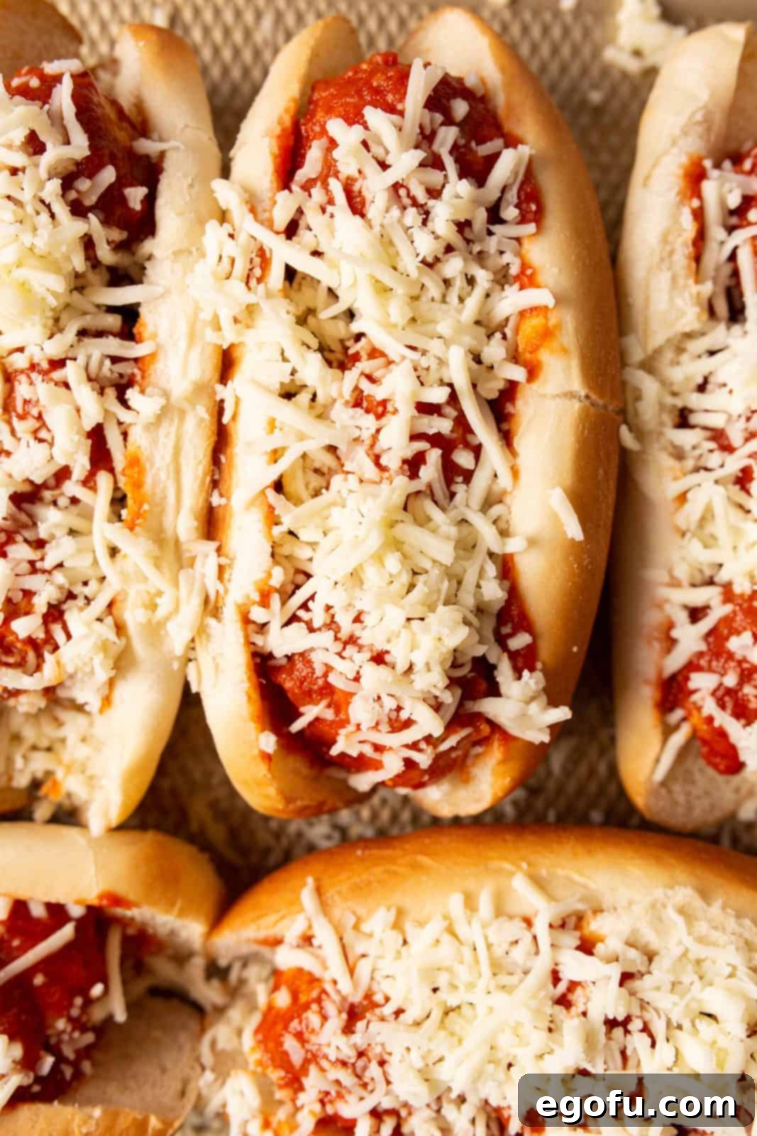 Cheese sprinkled on meatballs in buns.