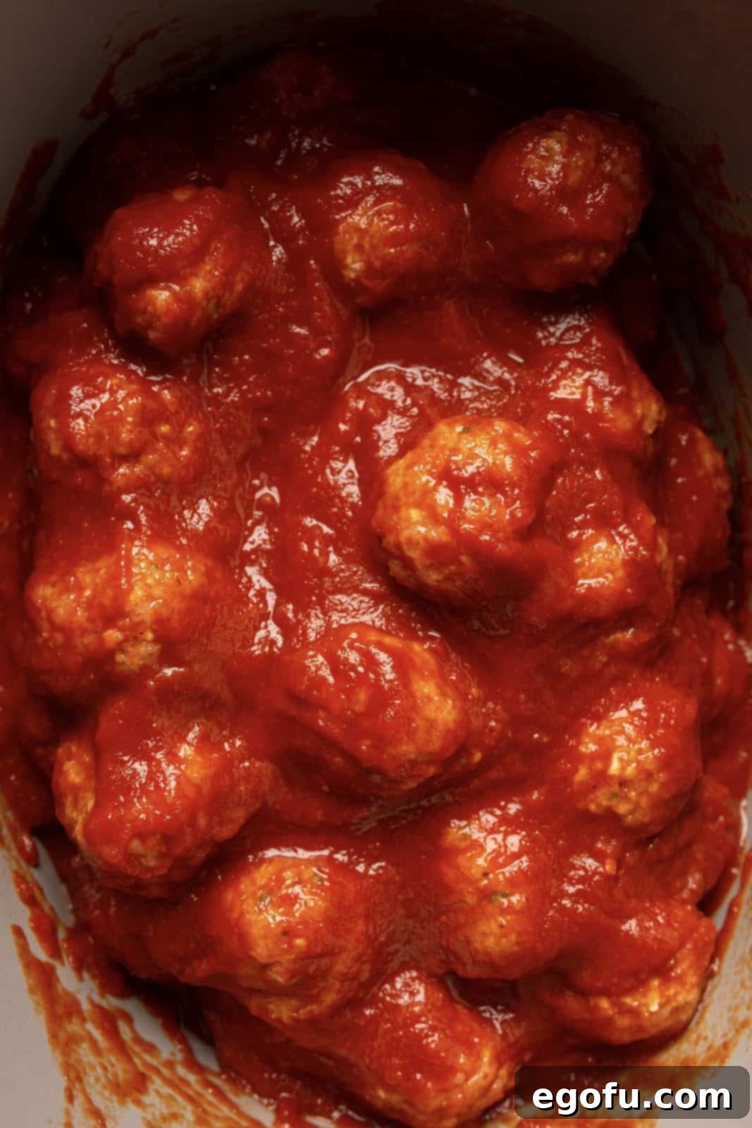 Remaining sauce being poured over the top of the meatballs in crock pot.
