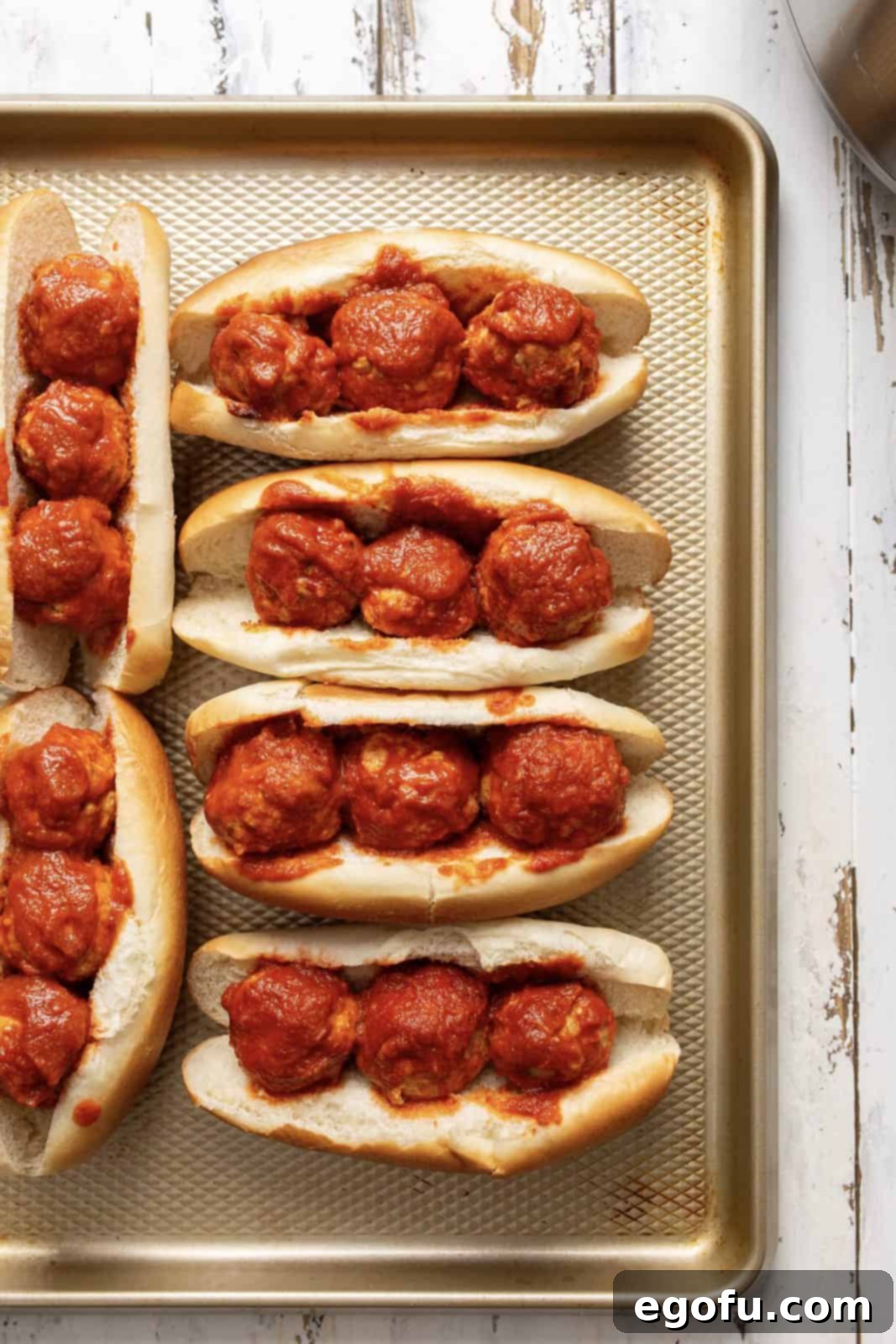 Meatballs placed on sub buns on baking sheet.