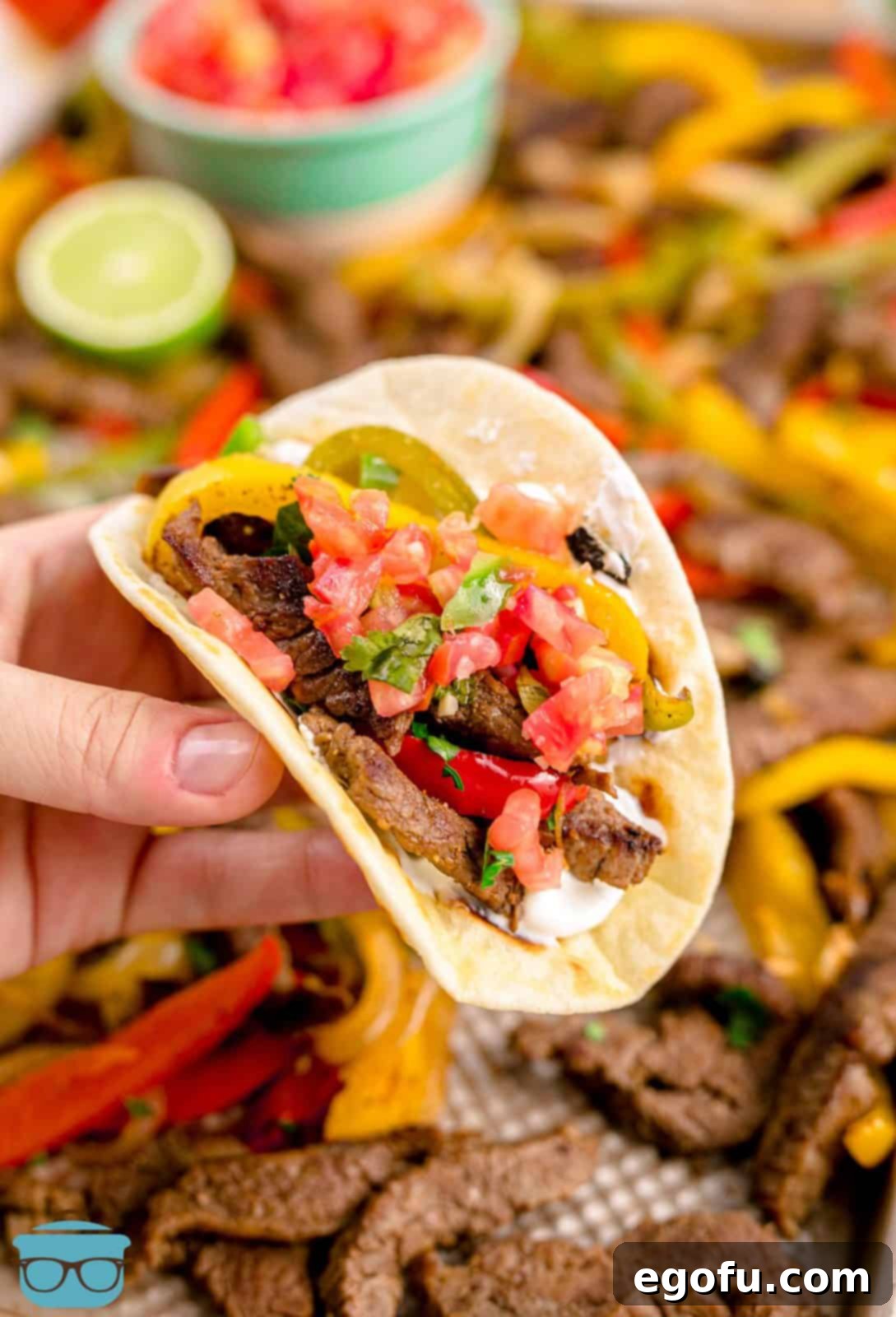 Hand holding up a warm tortilla filled with delicious Sheet Pan Beef Fajitas, showcasing tender beef and colorful vegetables.