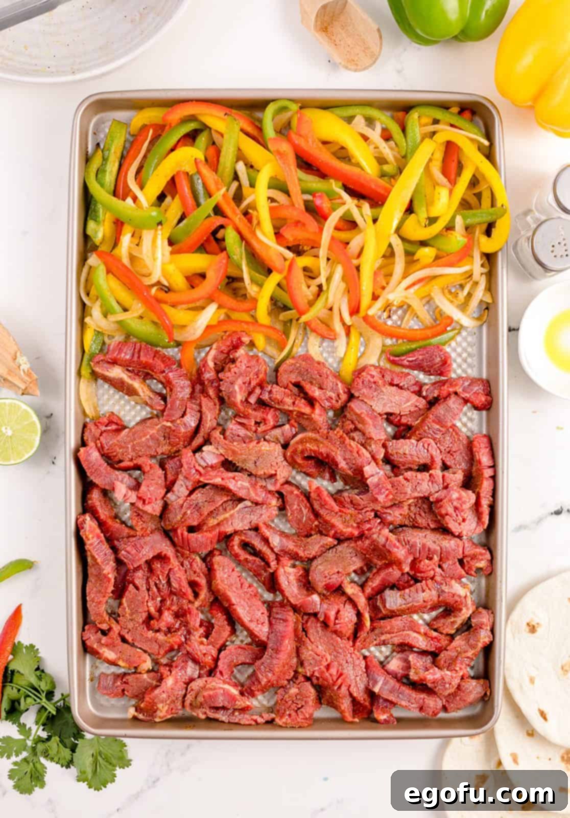 Seasoned beef strips added to the baking sheet alongside the partially cooked bell peppers and onions, ensuring both components cook perfectly.