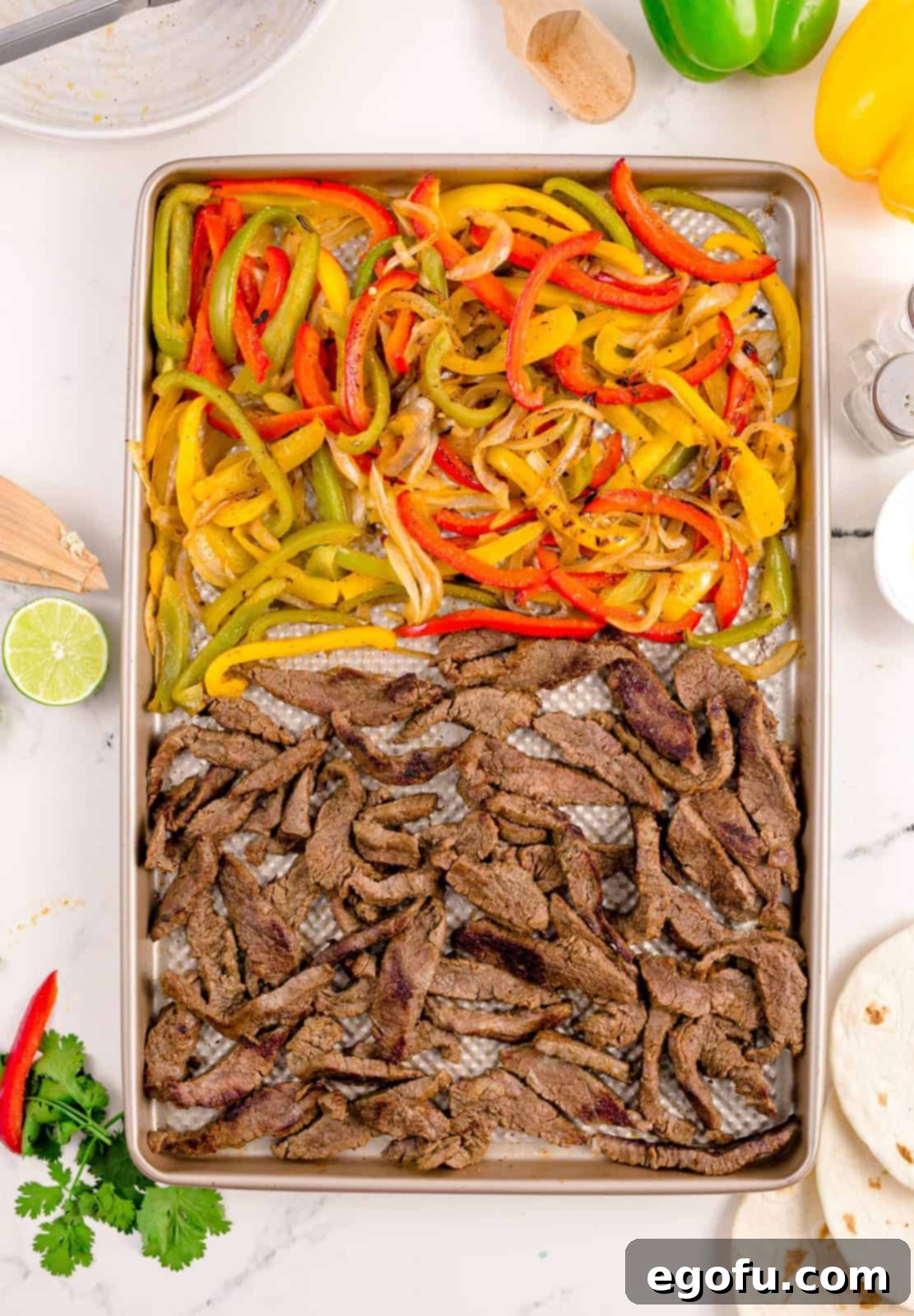 A completed sheet pan of beef fajitas, hot from the oven, with tender beef and beautifully roasted bell peppers and onions.