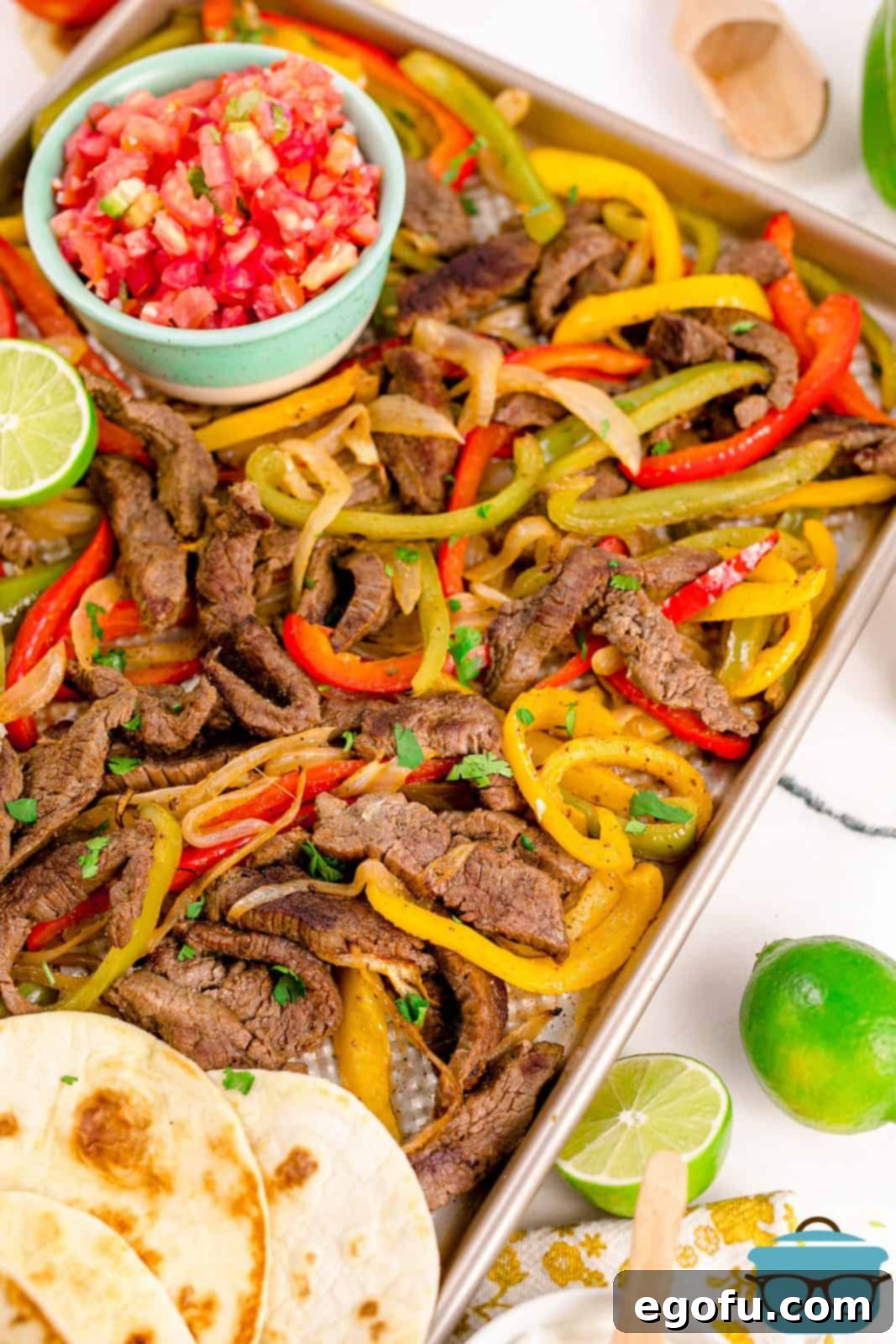 A vibrant spread of freshly cooked Sheet Pan Beef Fajitas on the baking sheet, surrounded by warm tortillas and an assortment of classic toppings like guacamole, pico de gallo, sour cream, and shredded cheese, ready for serving.