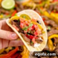 A squarer image of a hand holding up Sheet Pan Beef Fajitas in a tortilla, perfect for a recipe thumbnail.
