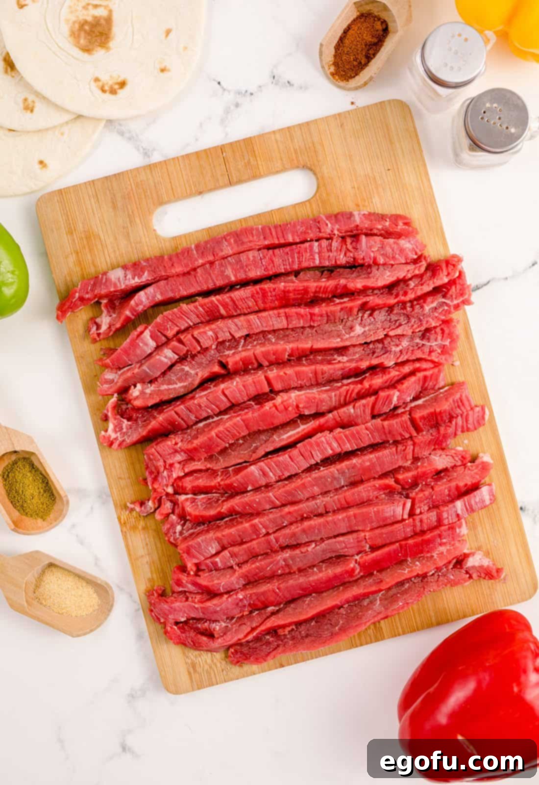 Thinly sliced flank steak arranged on a wooden cutting board, cut against the grain for tenderness.