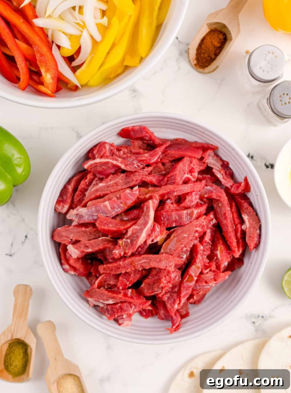 Sliced flank steak tossed with olive oil in a white ceramic bowl, ready for seasoning.