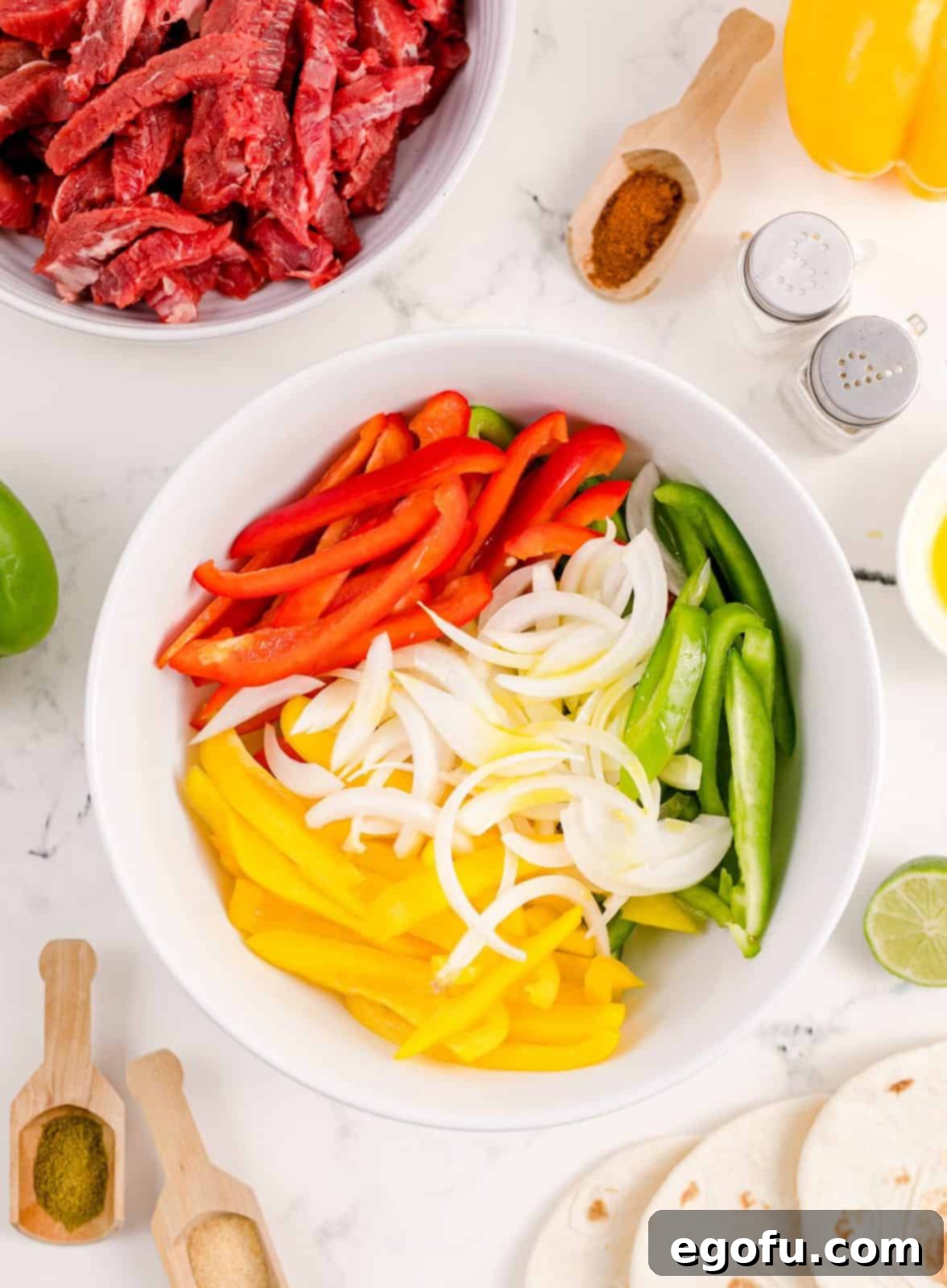Colorful assortment of thinly sliced bell peppers and onions coated in olive oil in a white bowl.