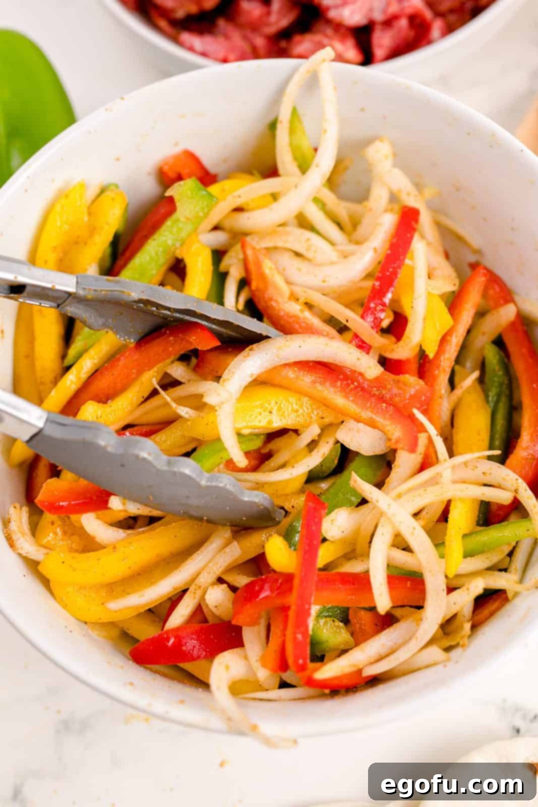 A spoon mixing the homemade fajita spice blend into the bowl of colorful bell peppers and onions.