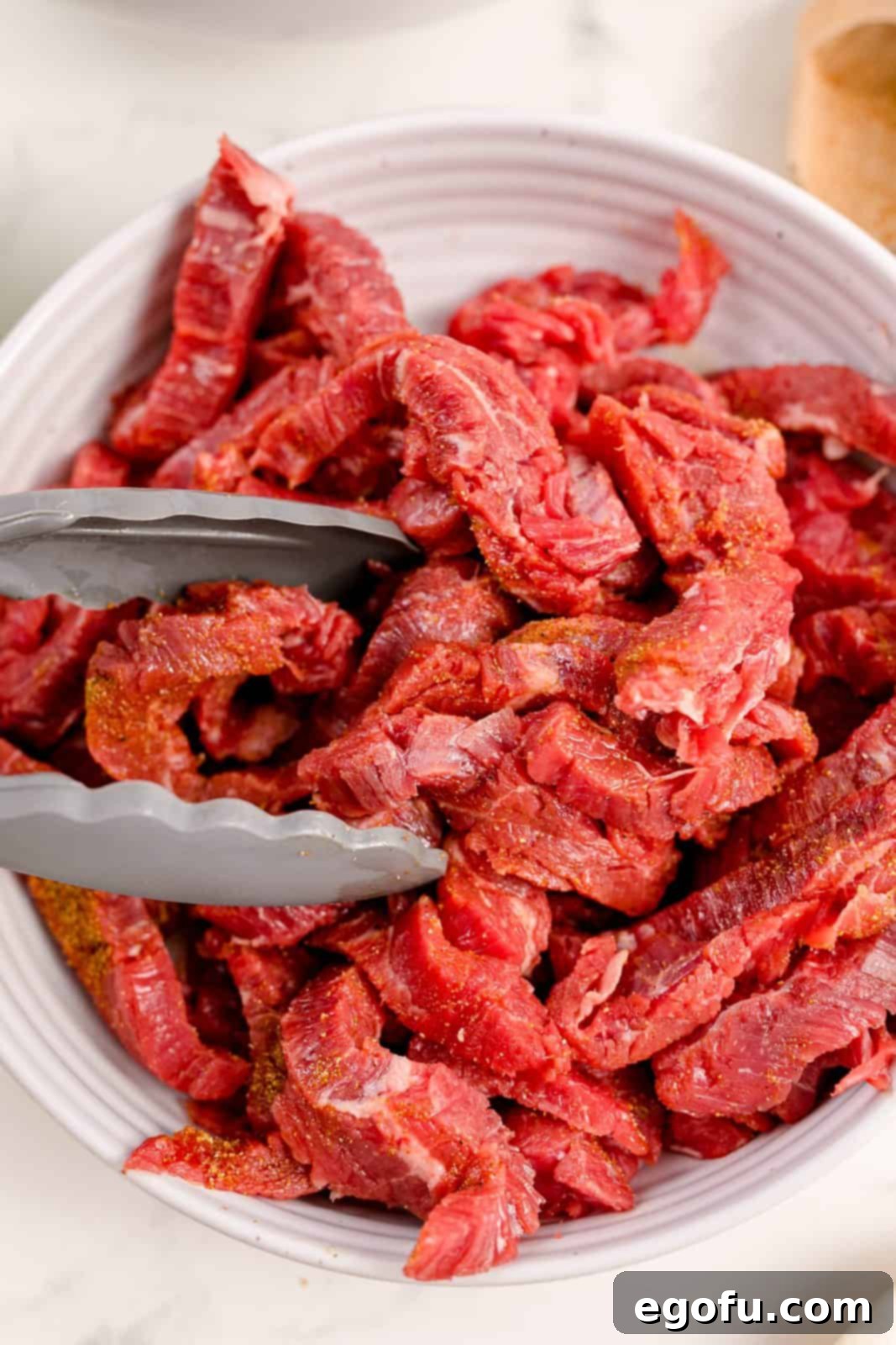 The remaining fajita spice blend being stirred into the bowl of thinly sliced beef.