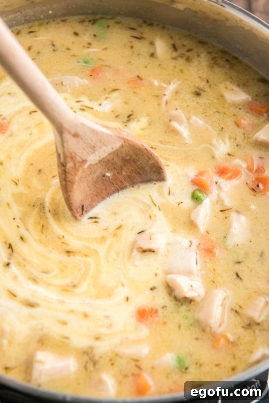 Heavy whipping cream being poured into the skillet mixture and gently stirred with a wooden spoon.