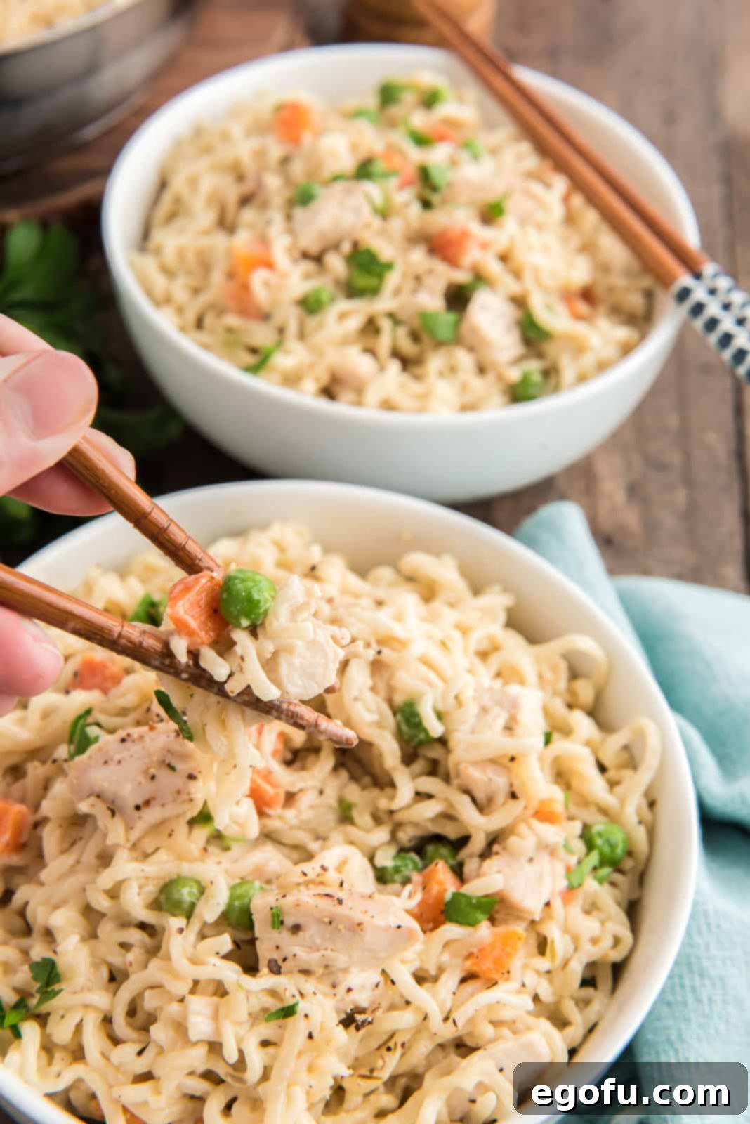 A bowl of Chicken Pot Pie Ramen being enjoyed, with a hand using chopsticks to pull out some of the delicious noodles and chicken.