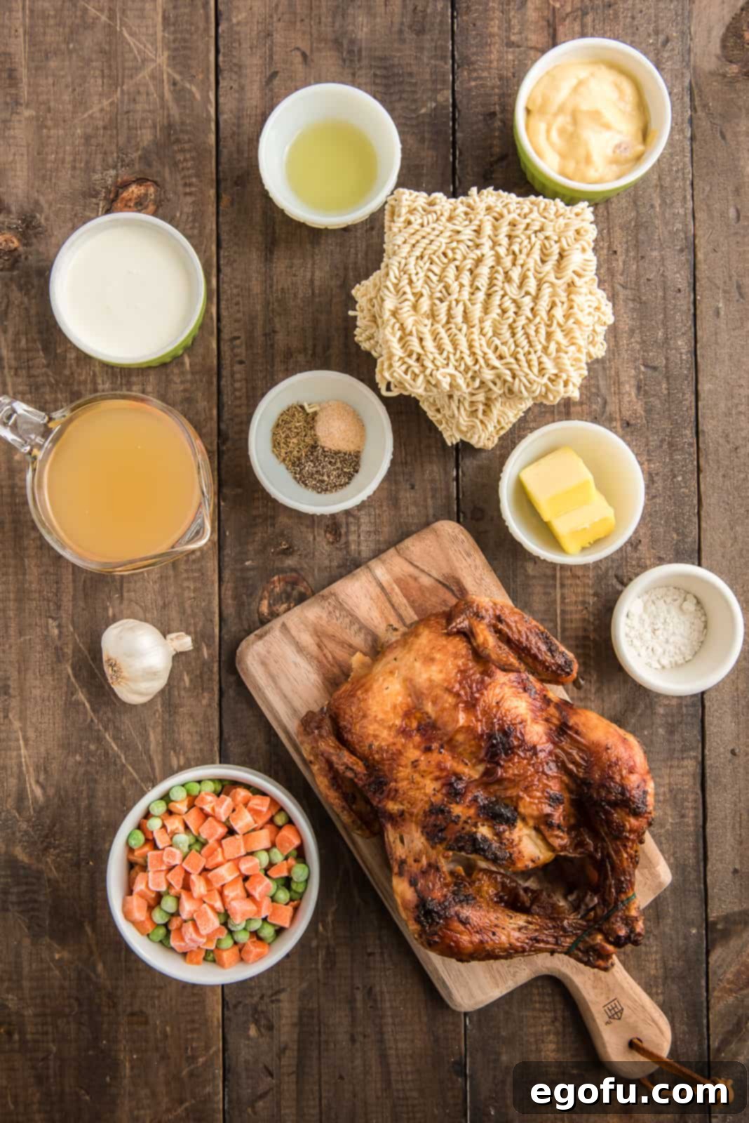 Ingredients needed: ramen noodles, salted butter, garlic, olive oil, frozen peas and carrots, garlic salt, pepper, thyme, flour, chicken broth, cream of chicken soup, rotisserie chicken and heavy whipping cream arranged on a wooden surface.