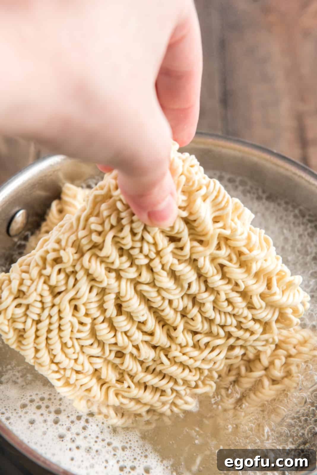 Hand adding ramen to boiling water.