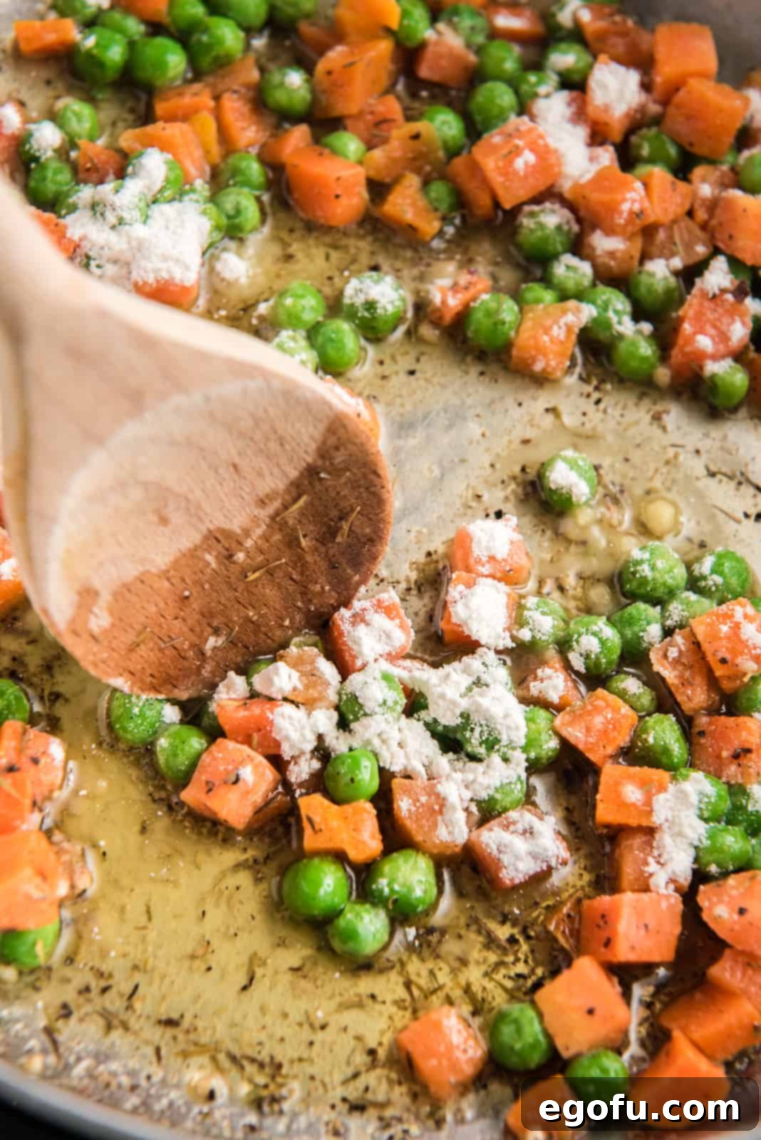 All-purpose flour being stirred into the skillet with sautéed vegetables, creating a roux.