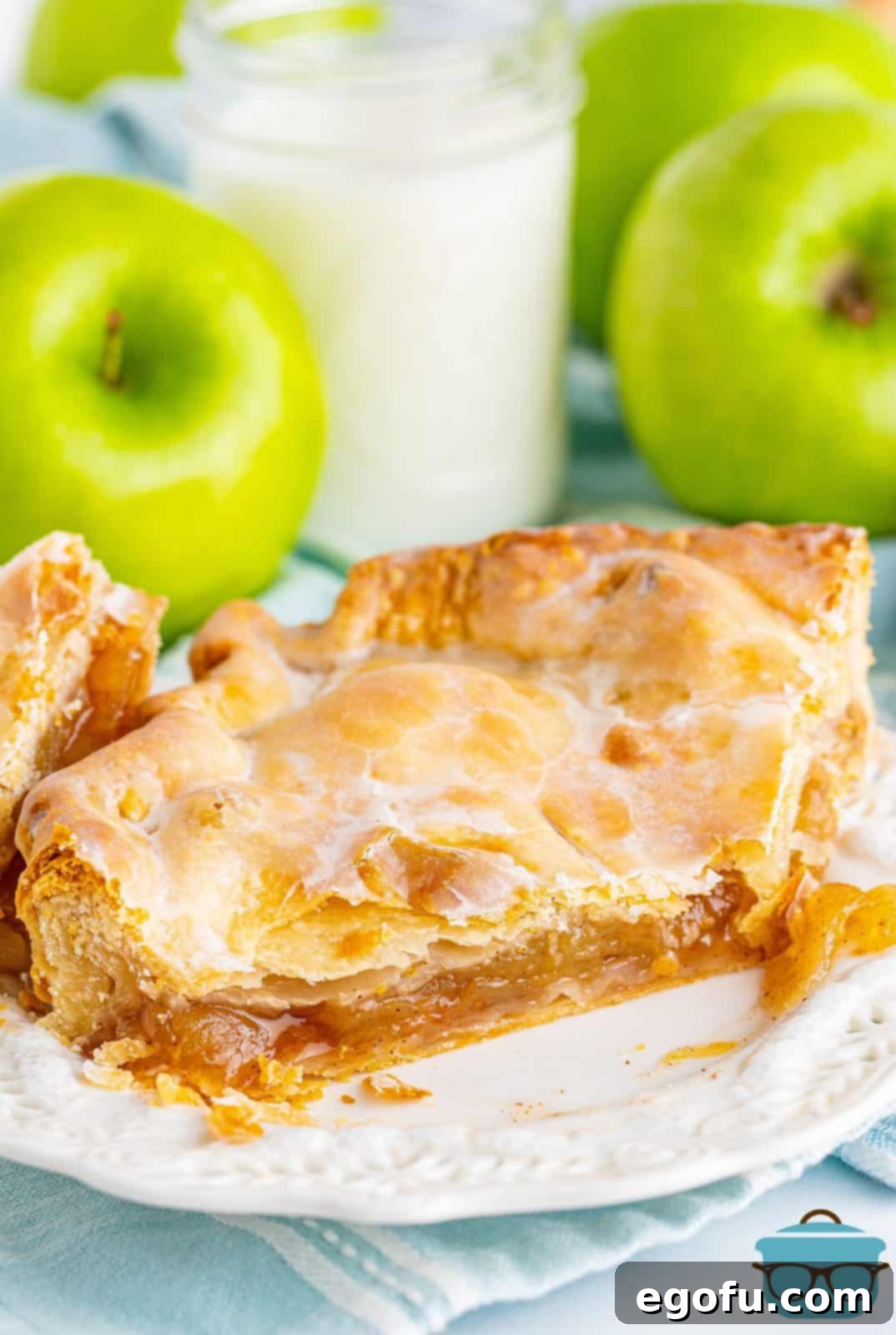 A perfectly baked slice of Apple Slab Pie on a white plate with a bite taken out, revealing the rich apple filling.