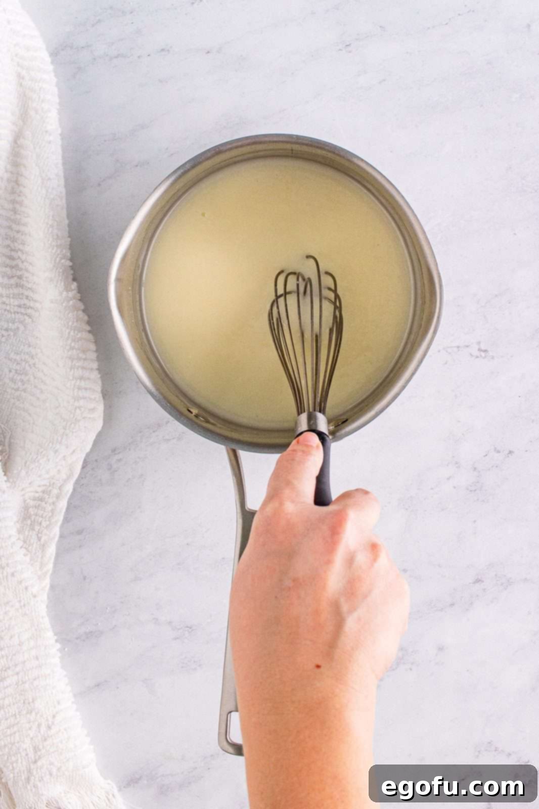 The smooth, sweet glaze mixture being whisked in a saucepan, ready to be applied.