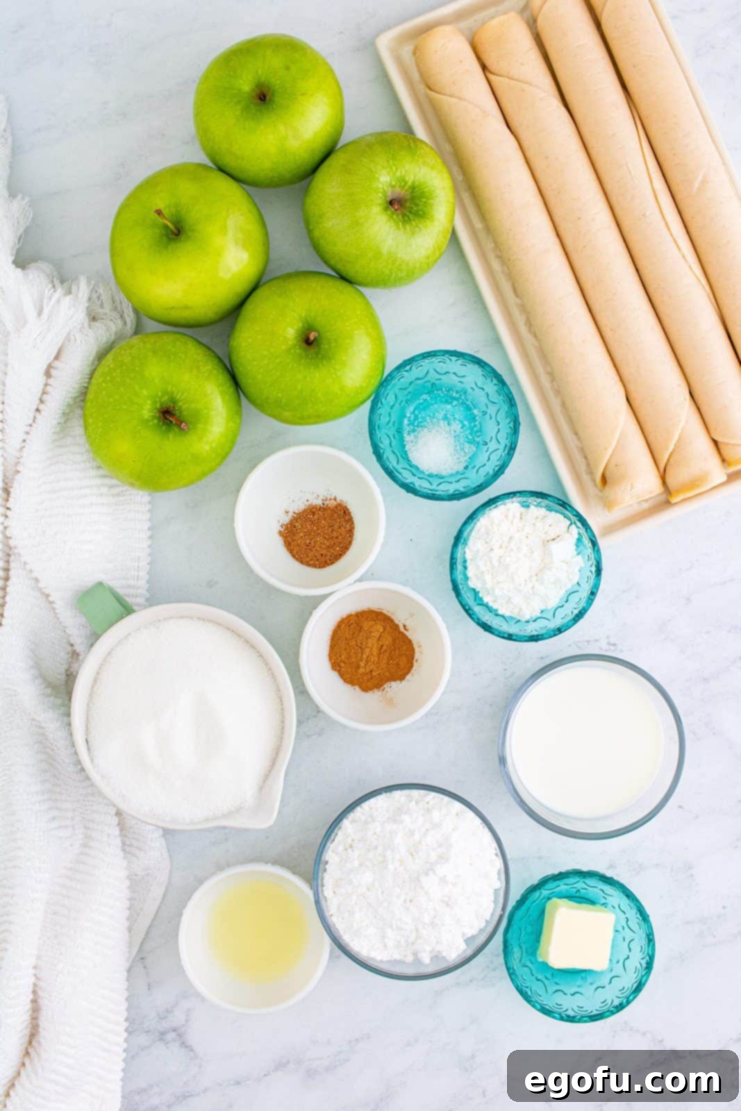 All the fresh ingredients for Apple Slab Pie: refrigerator pie crusts, apples, granulated sugar, cornstarch, lemon juice, ground cinnamon, ground nutmeg, salt, whole milk, salted butter, and powdered sugar.