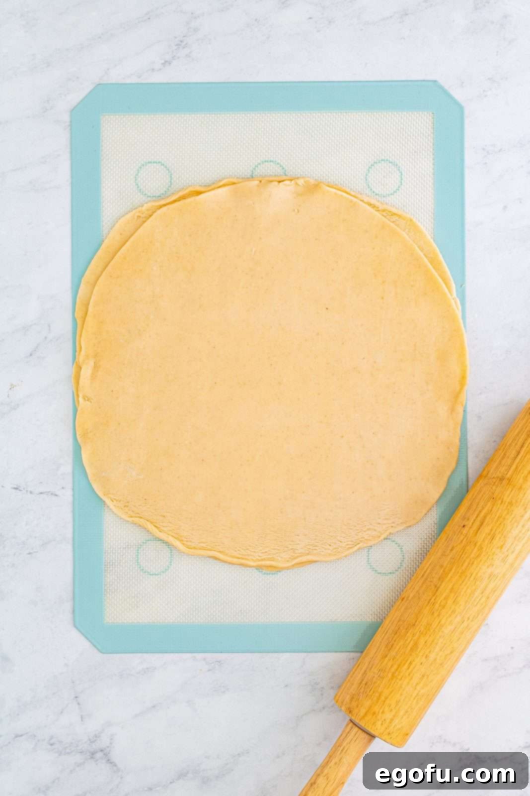 Two pre-made pie crusts ready to be rolled out on a baking mat.