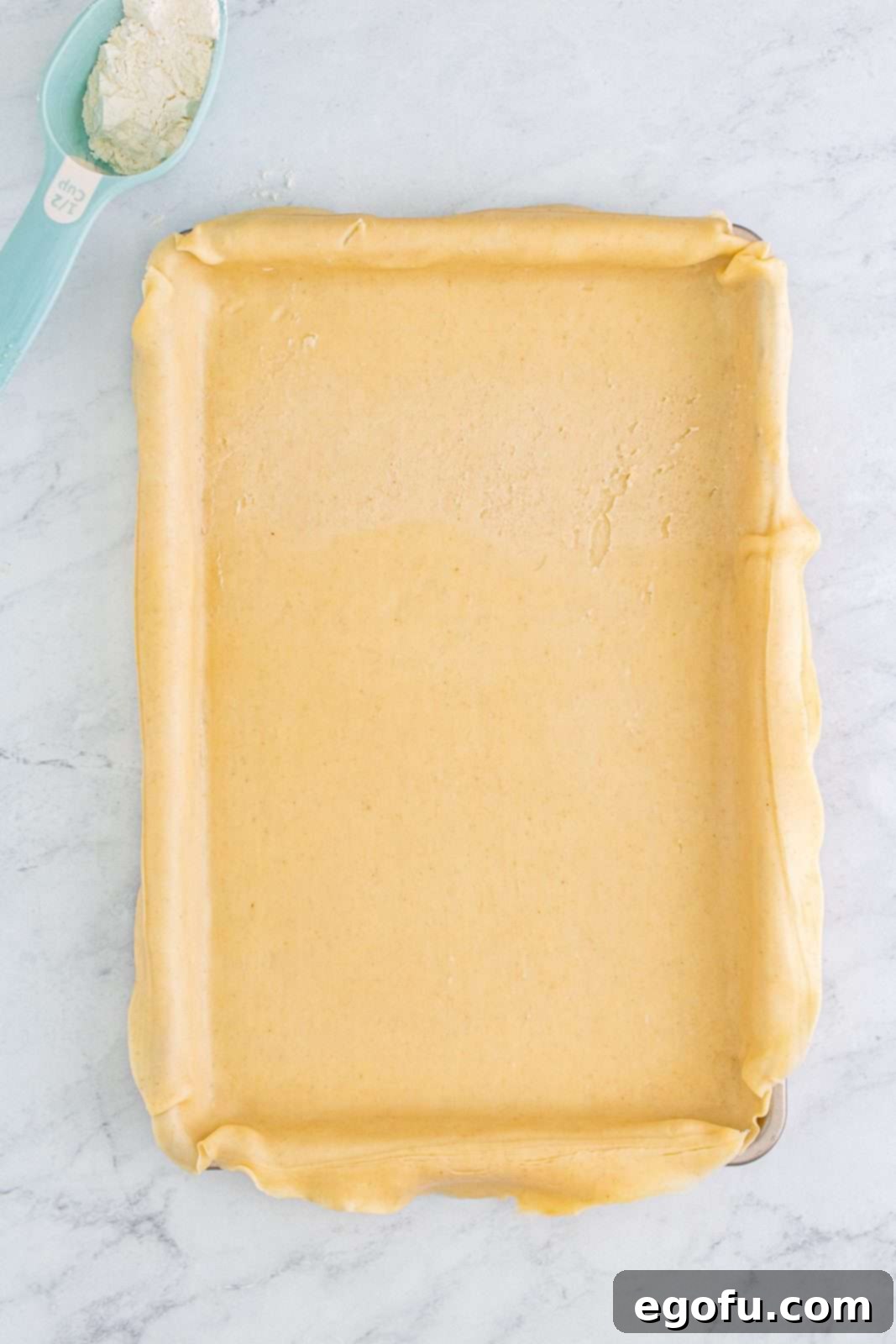 The rolled-out bottom pie crust expertly placed into a jelly roll pan, with edges overlapping.