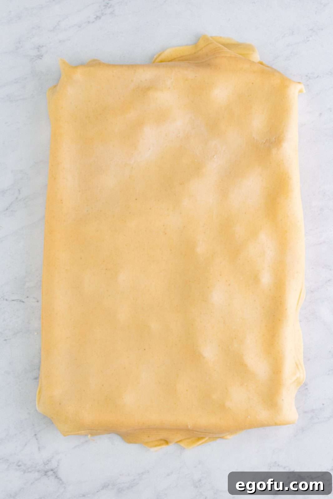 The second layer of rolled-out pie crust placed over the apple filling, completing the raw pie.