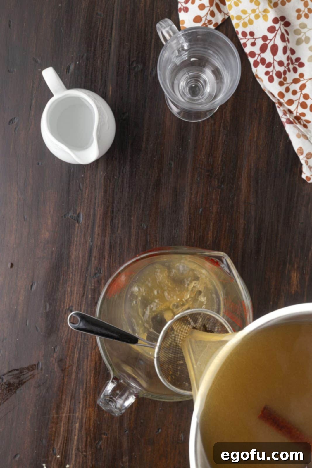 The spiced cider ingredients being strained through a fine mesh strainer to remove all whole spices.