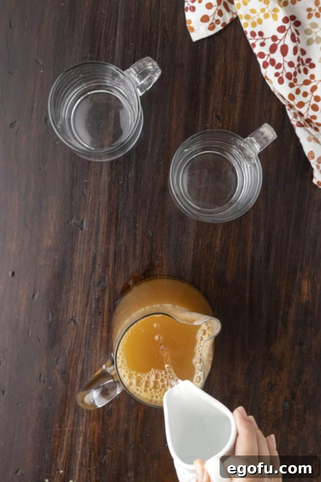 Vodka being poured into the warm, strained apple cider mixture in a saucepan.