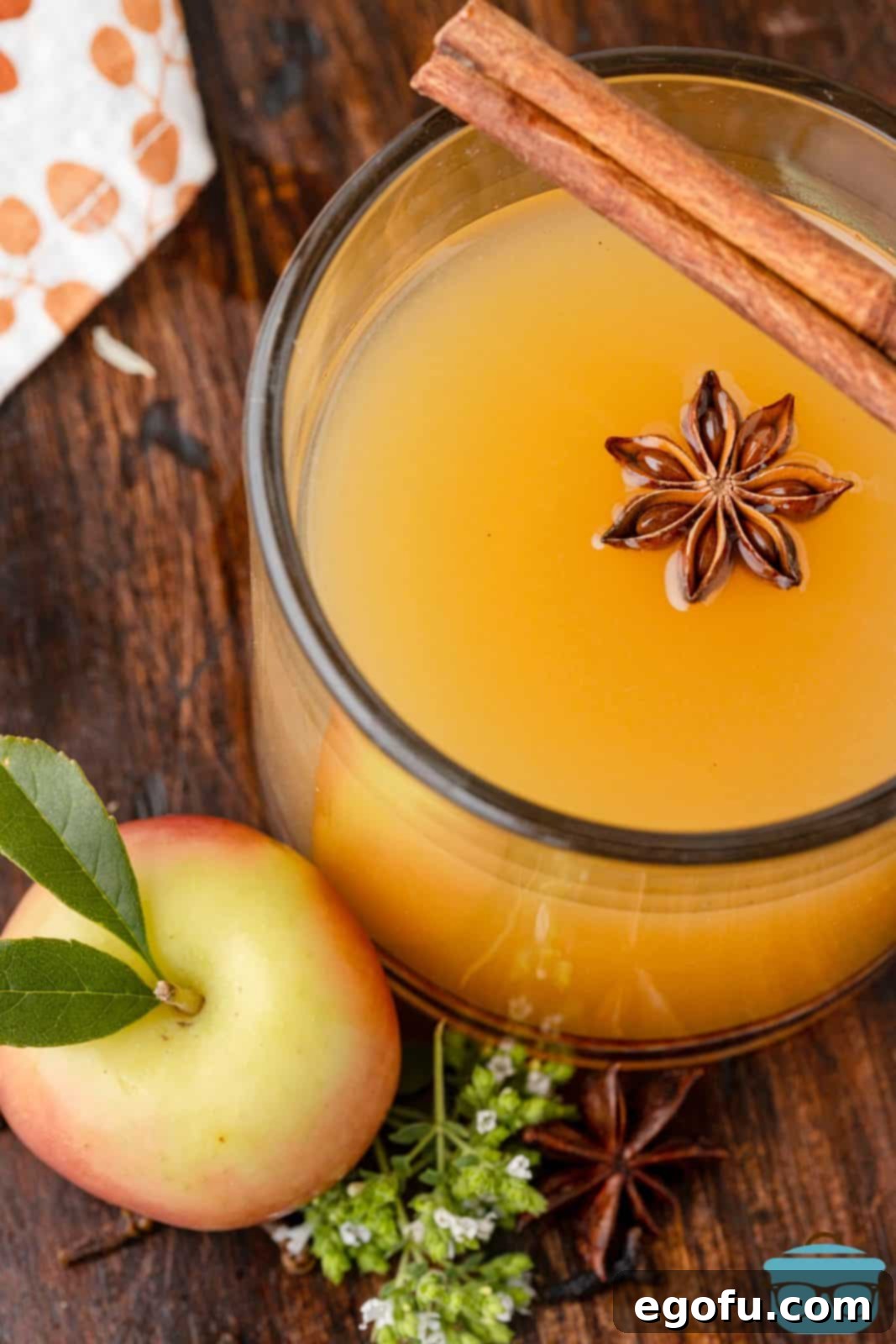 An overhead shot of a Warm Apple Cider Cocktail in a glass with garnishes next to a fresh apple, showcasing the festive appeal.