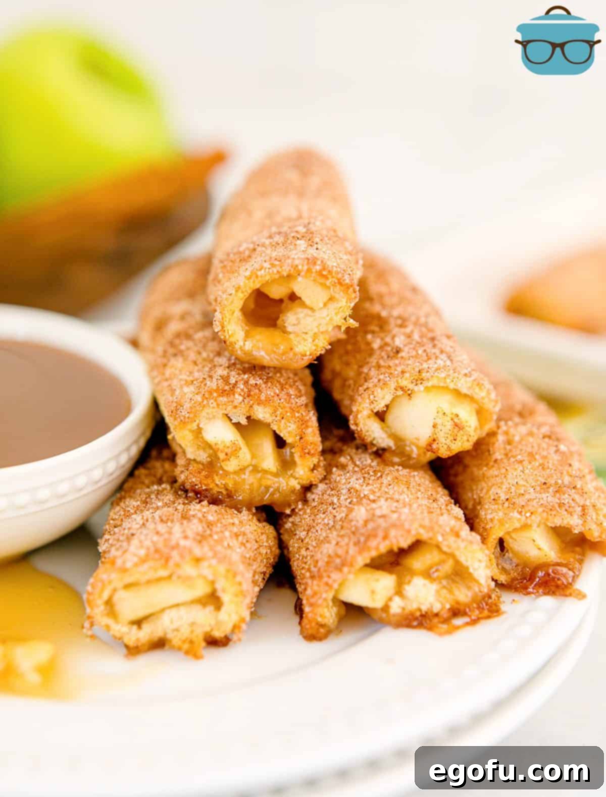 Stacked Baked Apple Pie Rollups on a plate with a drizzle of rich caramel sauce, showcasing their golden-brown crust and inviting texture.