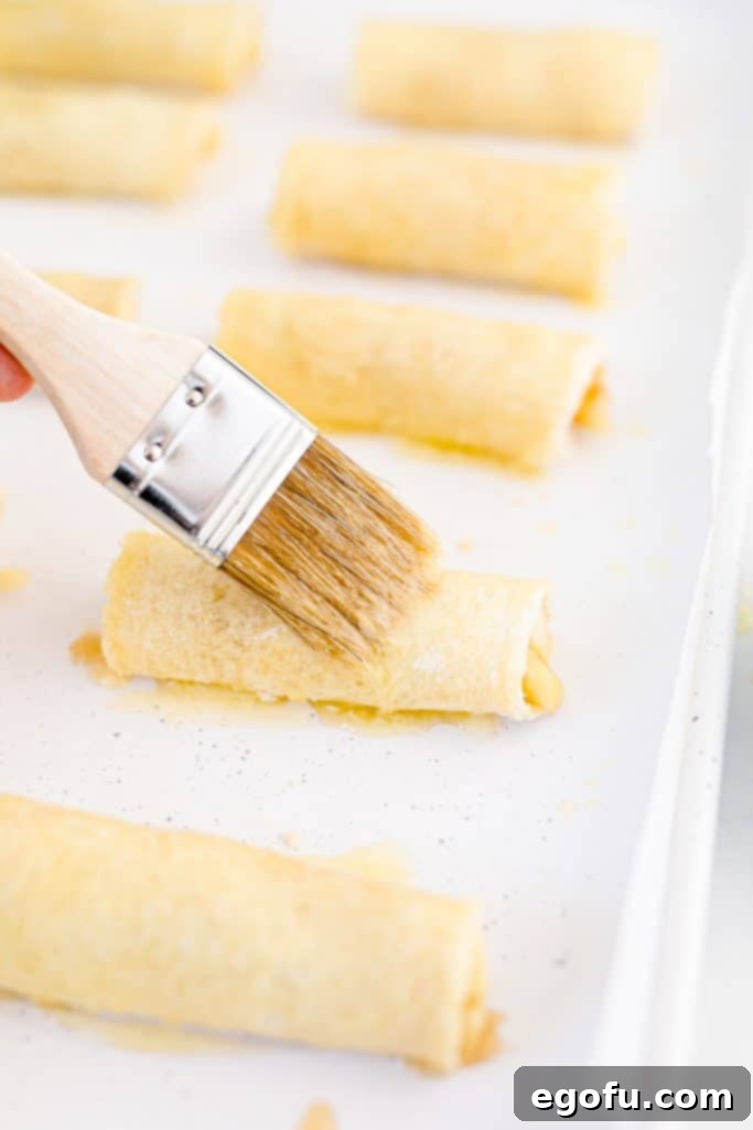 A rolled-up bread segment being delicately brushed with melted butter using a pastry brush, preparing it for the sugar-cinnamon coating.
